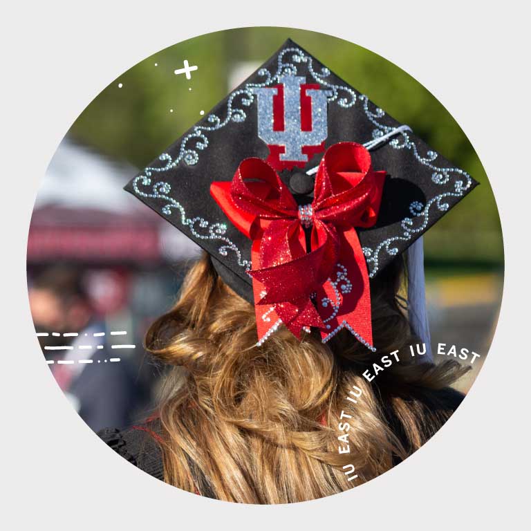 A student at commencement wearing a mortarboard with the IU trident on it.