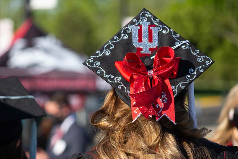 a student at commencement wearing a mortarboard with an IU trident on it.
