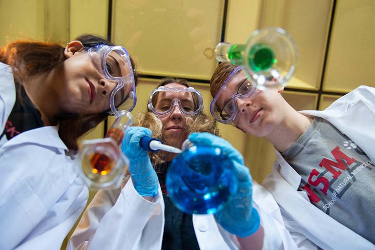 three IU East students look down at an experiment in progress