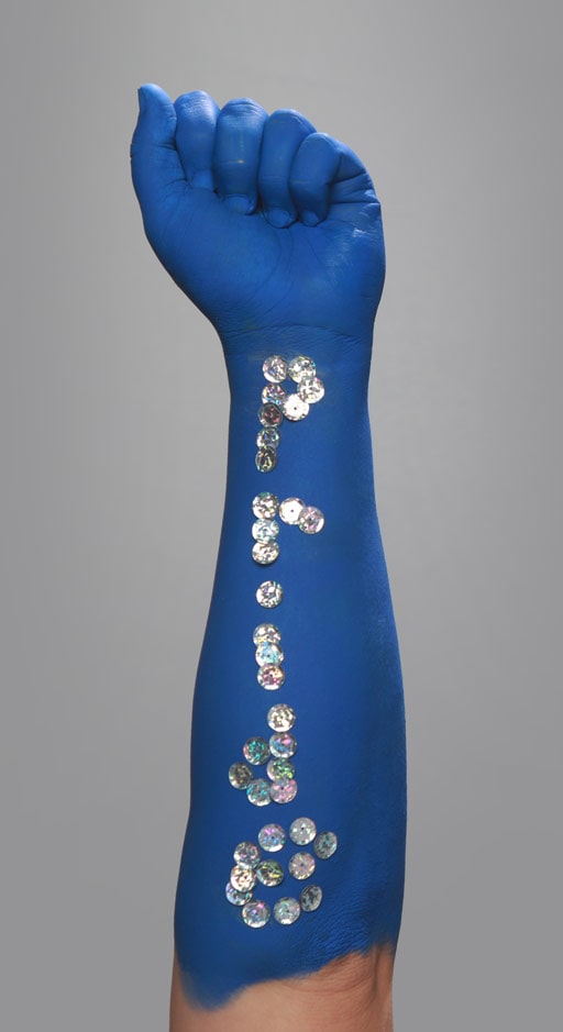 A fist high in the air with 'pride' spelled out in sequins on an arm painted blue.