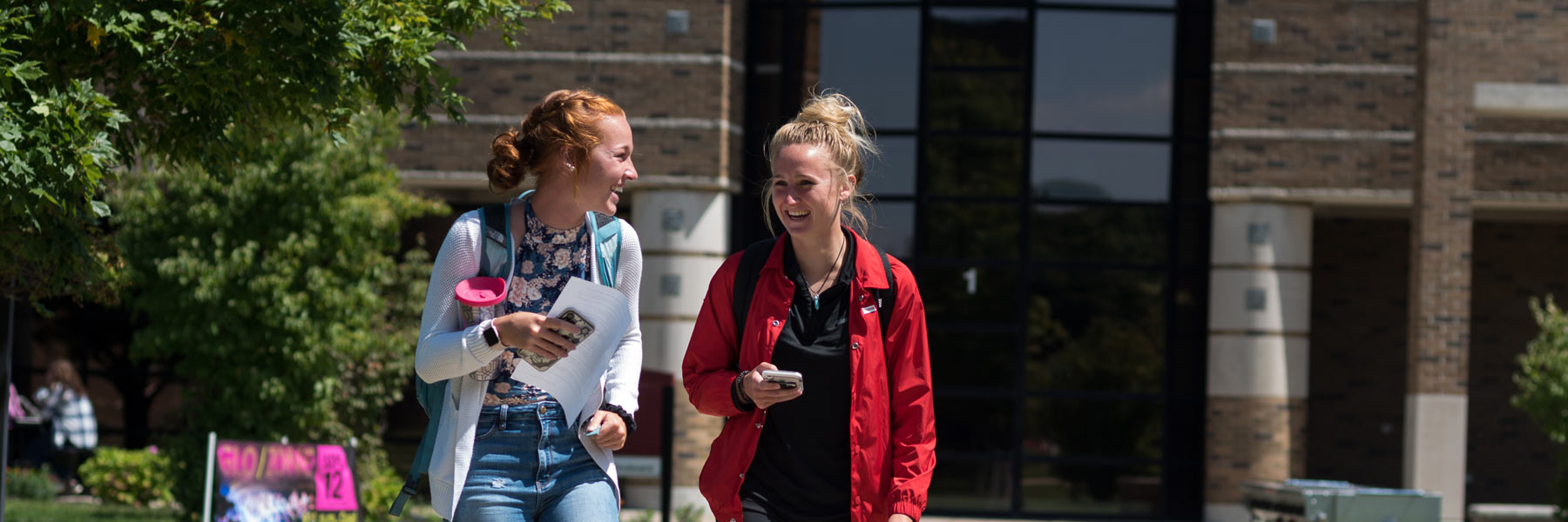 Two students smiling and laughing together while walking on-campus.