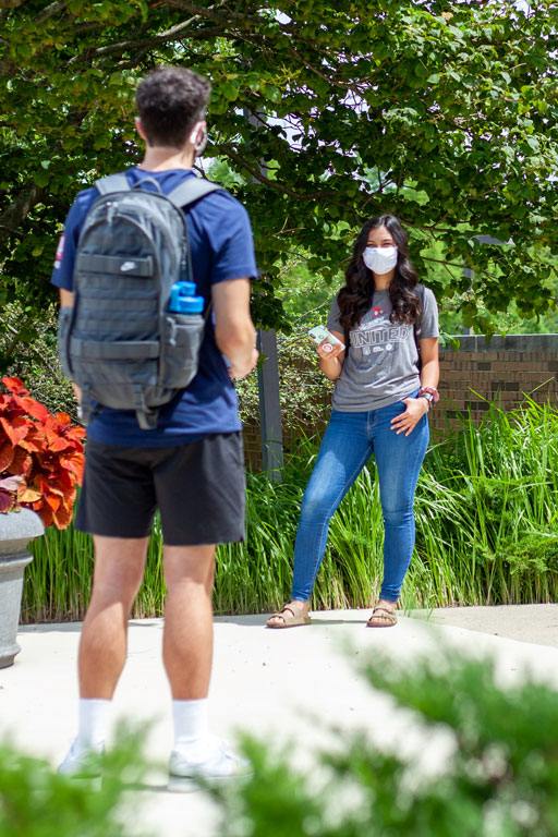 Students outside of Hayes Hall socializing while wearing masks and social distancing.